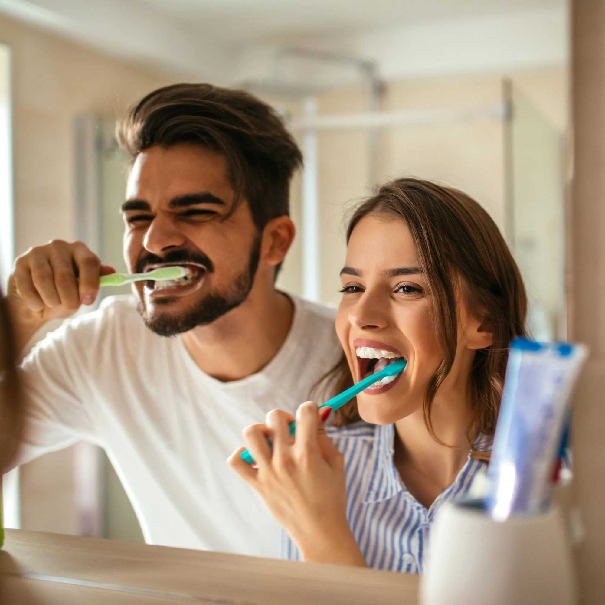 A couple brushing their teeth together in front of a bathroom mirror